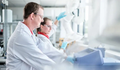 Zwei Mitarbeiter von REMONDIS – ein Mann und eine Frau – mit weissem Kittel und Schutzbrille bei der Arbeit in einem Prüflabor